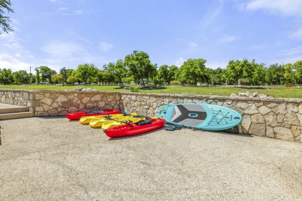 Des kayaks et une planche à pagaie sont posés près d’un mur de pierres dans un parc.
