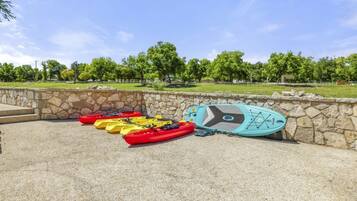 Des kayaks et une planche à pagaie sont posés près d’un mur de pierres dans un parc.