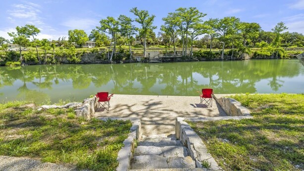 A serene lakeside view with steps leading to a dock, two red chairs, and a clear sky. - RENOVATED-Vacation Cabin, Riverfront - Hunt, TX (Ingram)