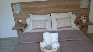 Een net opgemaakt bed met een bruine sprei, twee kussens met een golfpatroon, en een mandje met opgevouwen handdoeken op het bed.