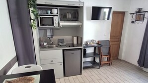 A compact kitchen with a microwave, sink, and small refrigerator. There is a dining area with a table and chairs, and a TV mounted on the wall.