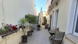 A narrow outdoor corridor with potted plants and a table with chairs.