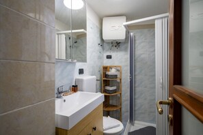 A modern bathroom with a marble sink, a toilet, a shower, and a built-in shelf with storage. - Casa Ravanas - City Center Studio (Bari)