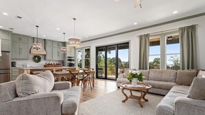 A spacious living room with a large sofa set, a dining area with wooden chairs, and a kitchen with light green cabinets. - The Magnolia Ridge Retreat (Jasper)