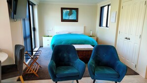 Een slaapkamer met een bed, twee blauwe fauteuils, een televisie, een schilderij en een kledingkast.