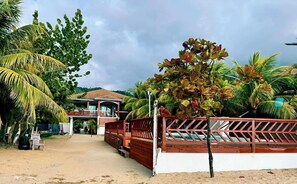 A beachfront property with a wooden deck, palm trees, and a house with a red roof. - Agua de Leon (Trujillo)