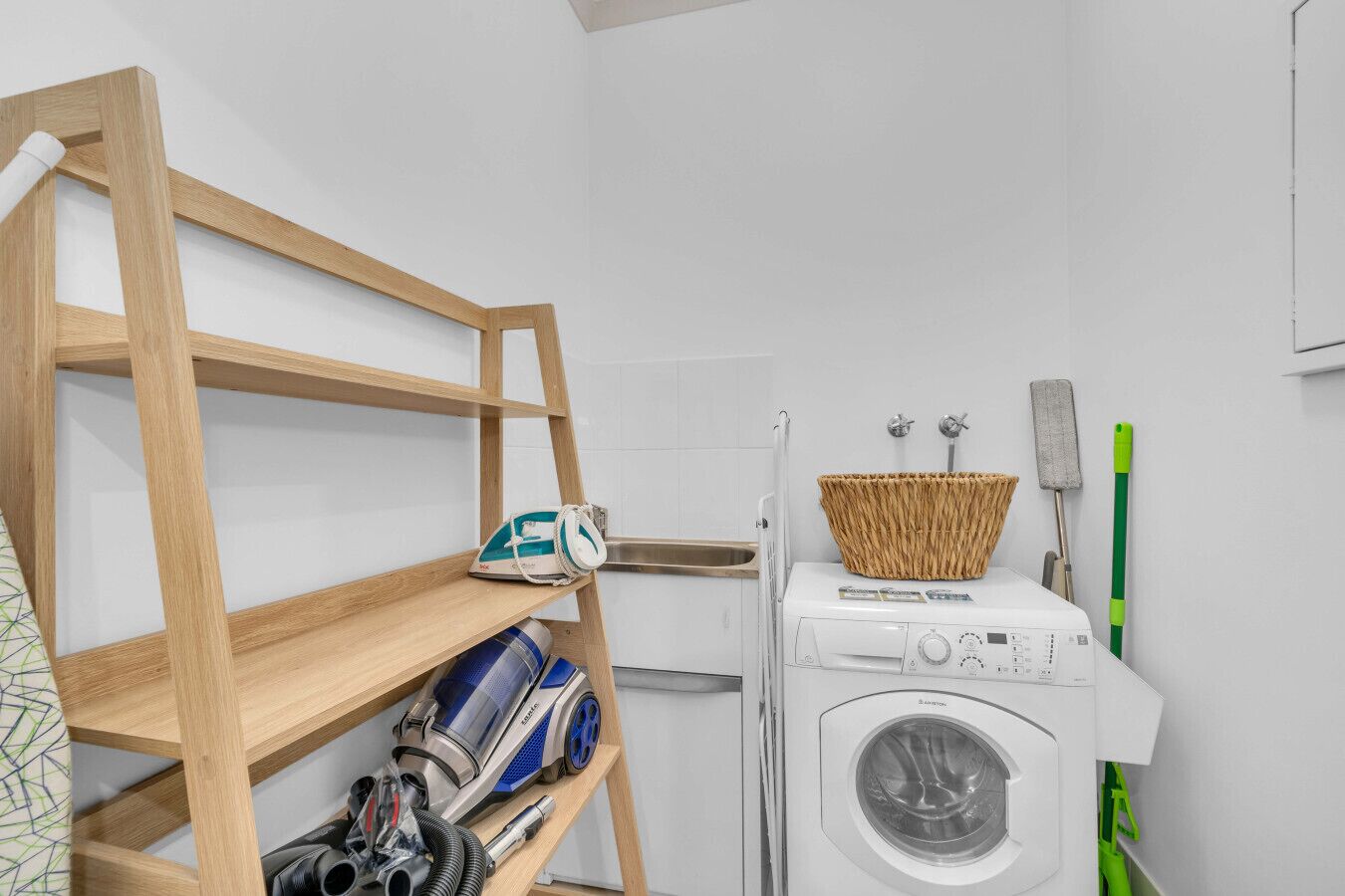 A laundry area with a washing machine, a dryer, a wooden shelf with cleaning supplies, and a basket on the dryer.