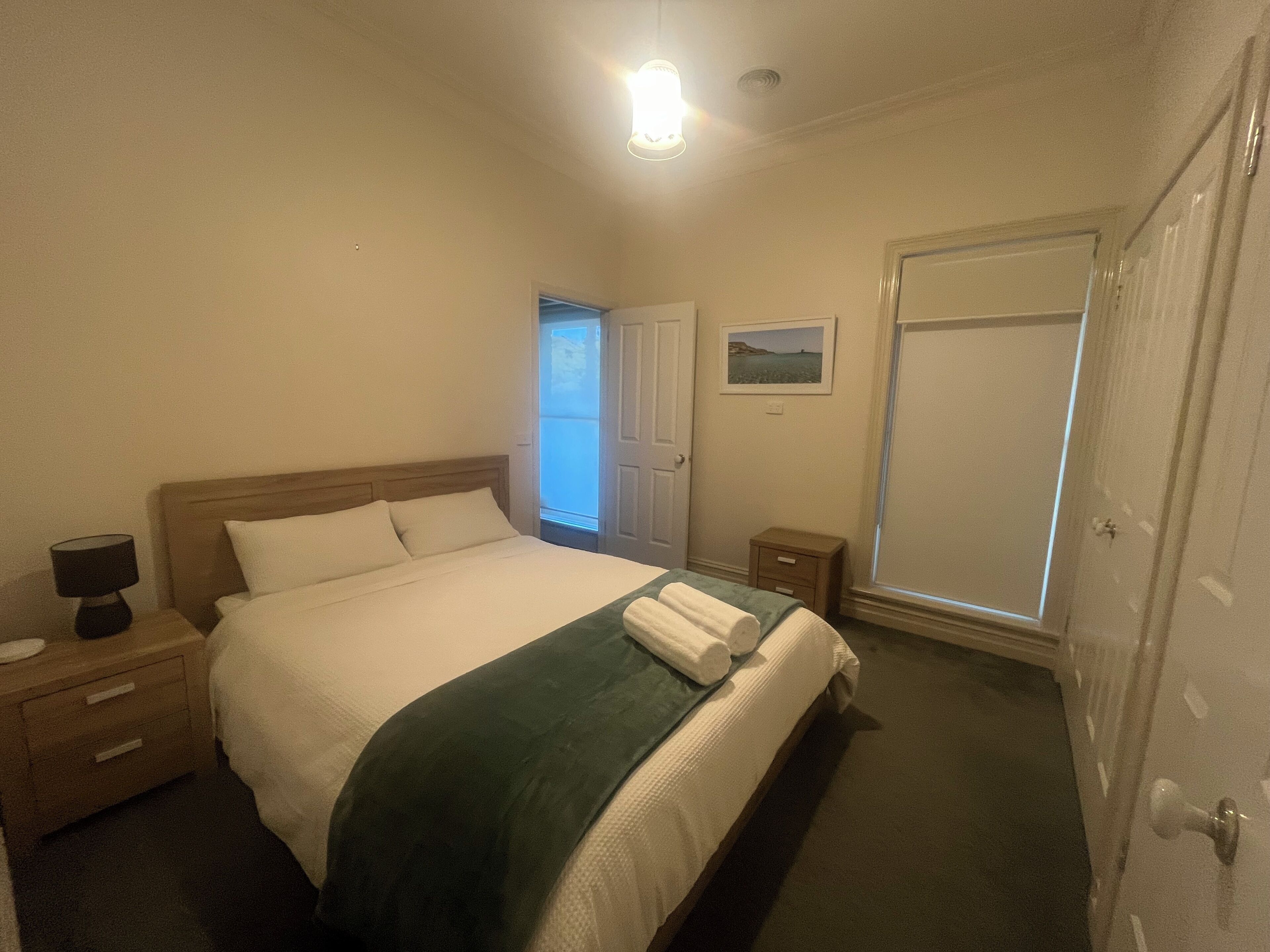 Ein ordentlich gemachtes Bett mit grüner Decke, einer Nachttischlampe und einem kleinen Nachttisch mit Schubladen.