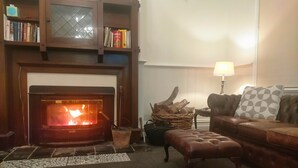 A cozy living room with a fireplace, a leather sofa, a coffee table, and a bookshelf. - Gather & Stay: The Honeysuckle Inn - Sleeps 14 in Style (Violet Town)