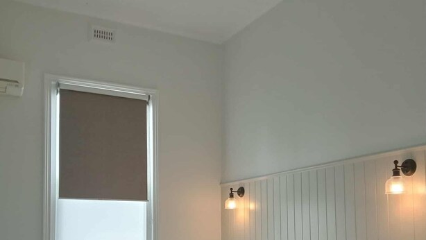 Un dormitori amb llit, finestra amb persianes, ventilador de sostre i il·luminació penjada a la paret.