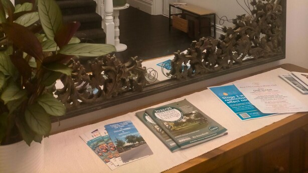 Un miroir avec un cadre orné, un escalier et un bureau avec des brochures.