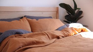 A bed with a wooden headboard, a large potted plant to the right, and a blanket with a blue pillow. - Indulgent stay in trendy Prahran (Prahran)