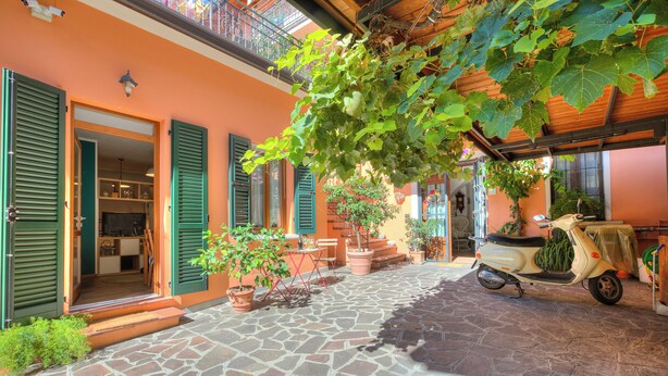 A courtyard with a stone floor, green shutters, a scooter, and potted plants. - Vicky Loft Gardone-relax & Vittoriale, Gardone Riviera, Italy (Gardone Riviera)