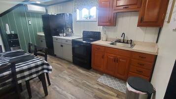 A compact kitchen with wooden cabinets, a black stove, and a dining area with a checkered tablecloth.