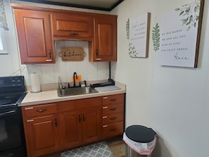 A kitchen with wooden cabinets, a stainless steel sink, a stove, and a trash bin.