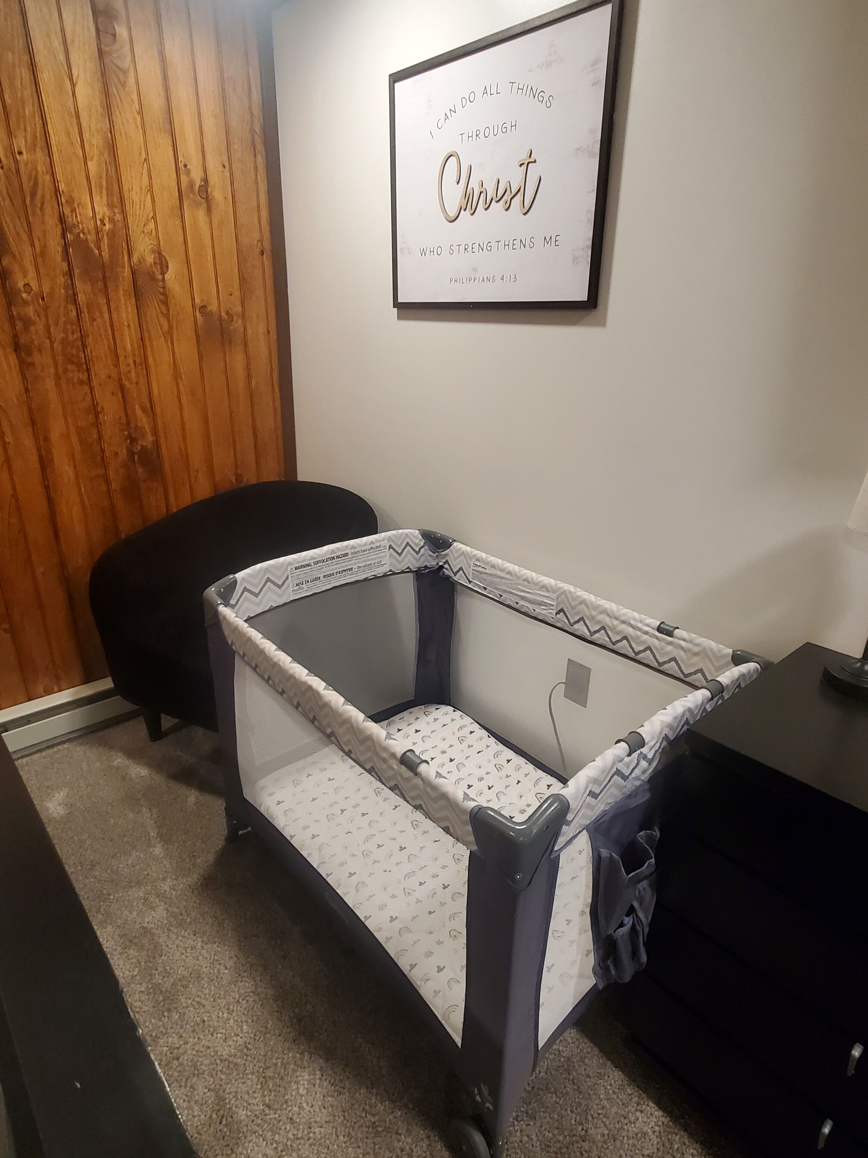 Un berceau pour bébé avec un matelas à motifs blancs et gris, un mur en bois, une citation inspirante encadrée et une chaise de bureau noire.
