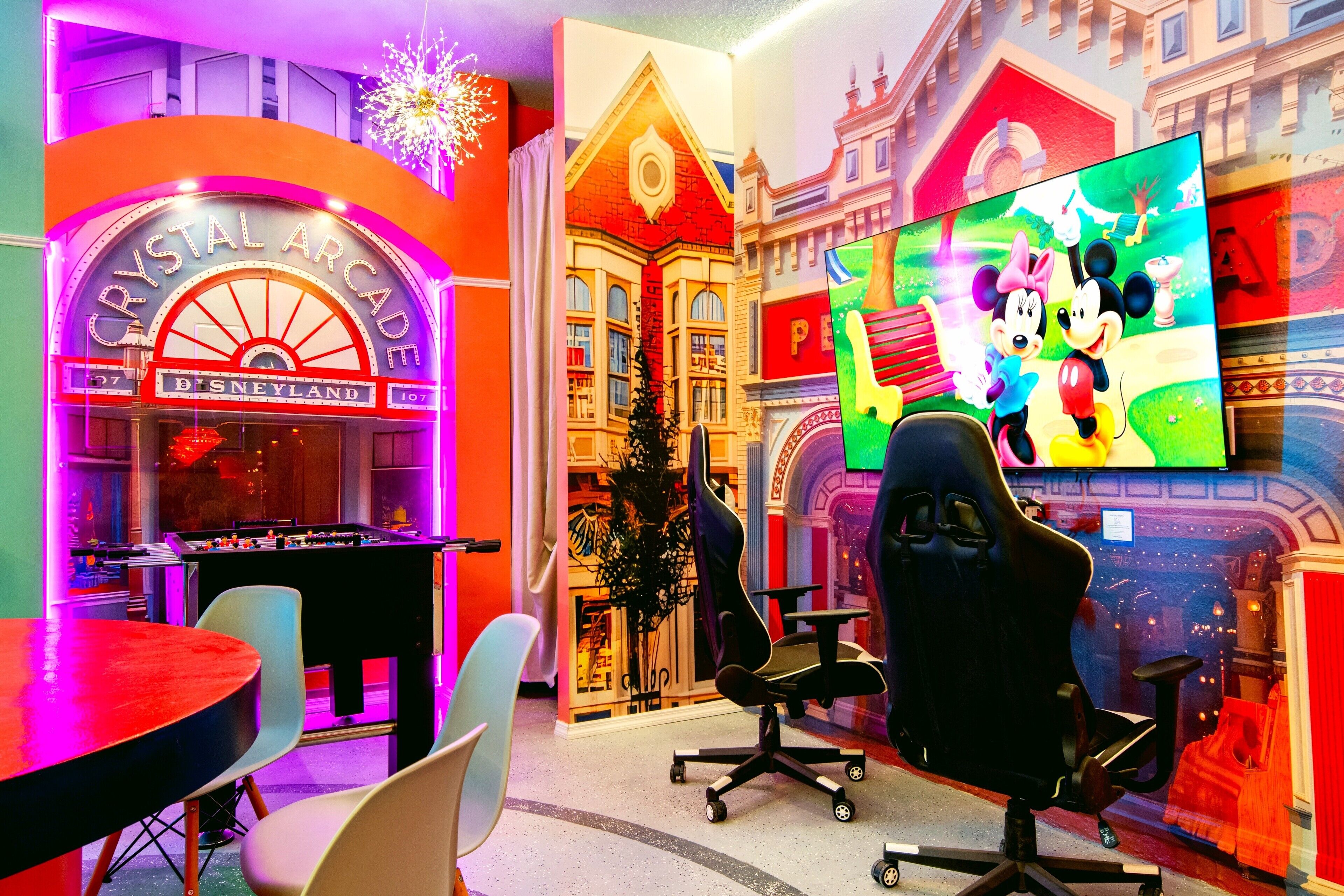 A room with a foosball table, a large TV screen, and a Disney-themed mural.