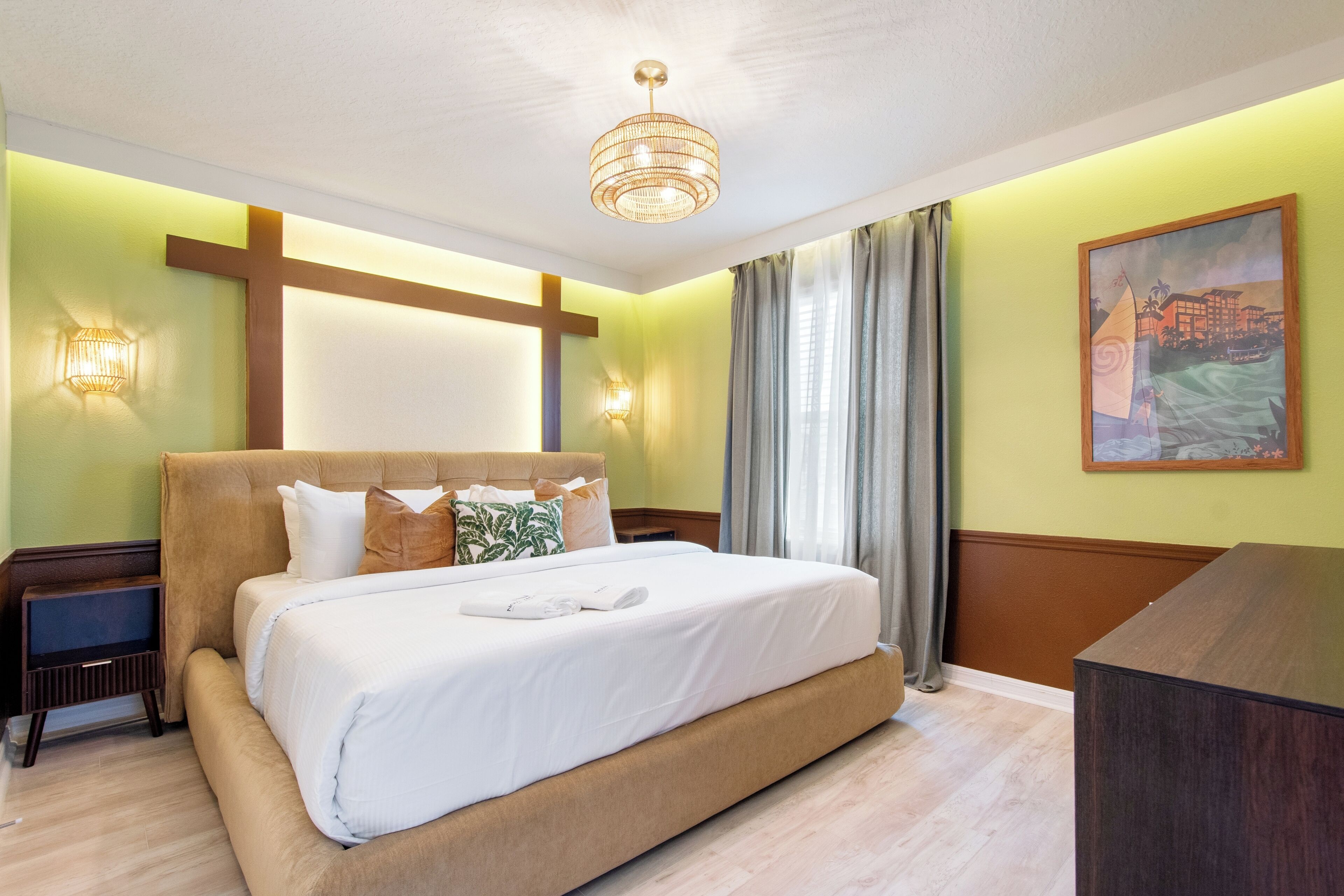 A hotel room with a large bed, a nightstand, a desk, a chandelier, a painting, and a window with curtains.