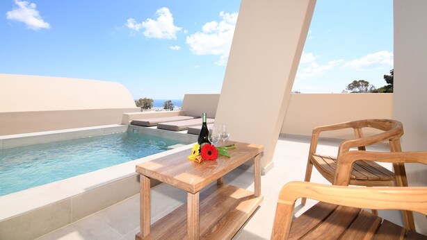 Una mesa de madera con una botella y copas junto a una piscina, con vistas despejadas al cielo y árboles lejanos.