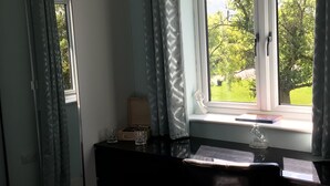 A room with a desk by a window, a mirror, a small wooden box, and a glass vase.