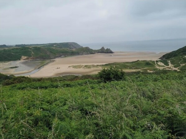 A coastal landscape with a sandy beach, green hills, and a clear sky.