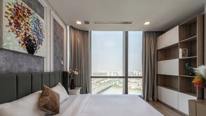 Una habitación de hotel moderna con una cama grande, vistas a la ciudad, una estantería y un cuadro abstracto de colores.