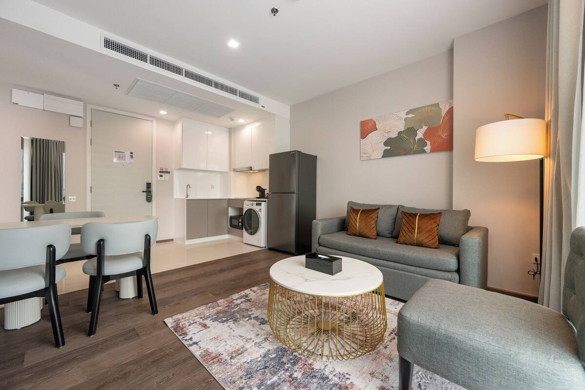 Un salon moderne avec un canapé gris, une table basse ronde et un coin repas comprenant une table et des chaises blanches.