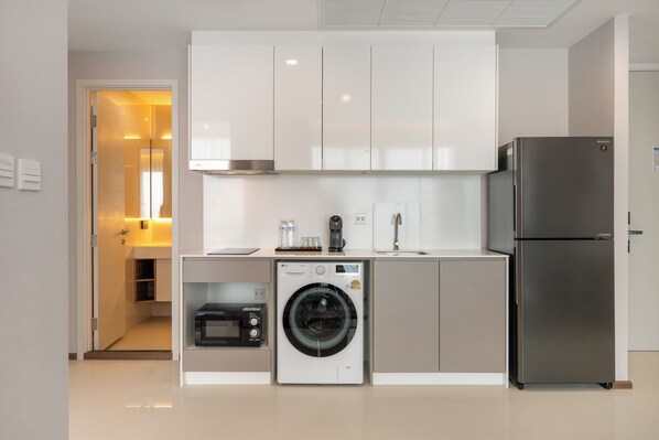 Una cocina compacta con lavadora integrada, refrigerador y microondas.