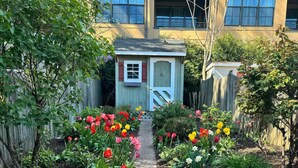 Un sentier de jardin mène à un petit abri de jardin avec une porte et des fenêtres rouges.