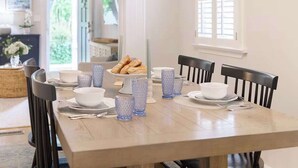 Une table à manger dressée avec de l’assiette et des bols blancs, ainsi que de la verrerie bleue, entourée de chaises en bois foncé.