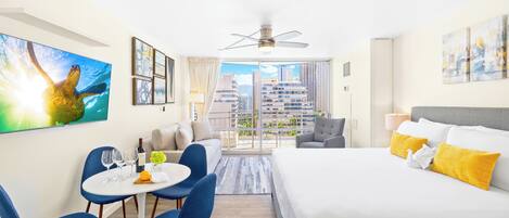 Habitación de hotel moderna con una cama, zona de comedor con sillas, una mesa y un amplio ventanal con vistas a la ciudad.