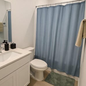 A bathroom with a white sink, a toilet, a blue shower curtain, and a green bath mat.