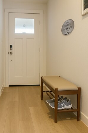 A hallway with a white door, a bench with shoes, and a sign on the wall.