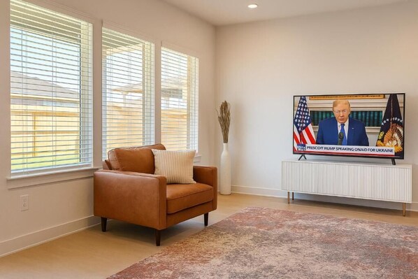 A living room with a brown leather sofa, a large flat-screen TV, and a white radiator.