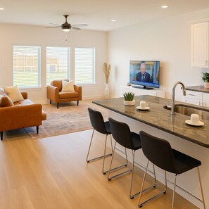 A modern kitchen with a central island, bar stools, a television, and a ceiling fan.