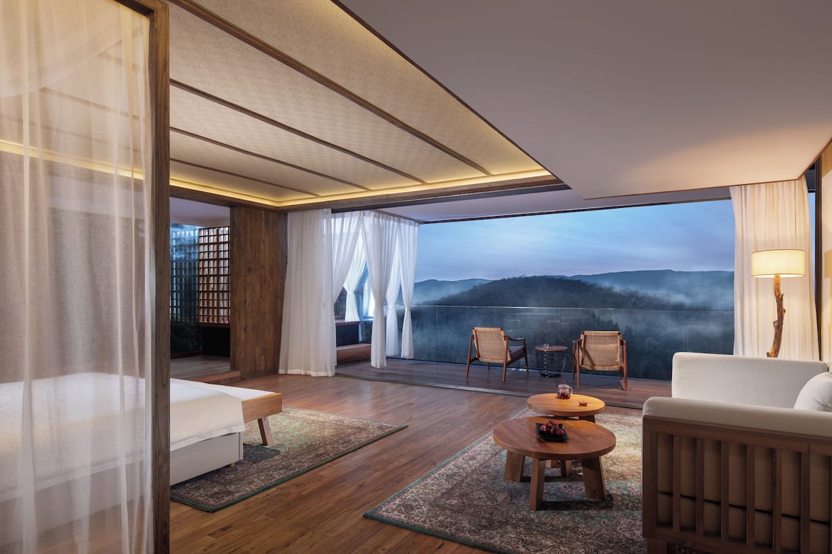 Una moderna camera d'hotel con balcone, pavimento in legno, divano, un tavolino e una lampada.