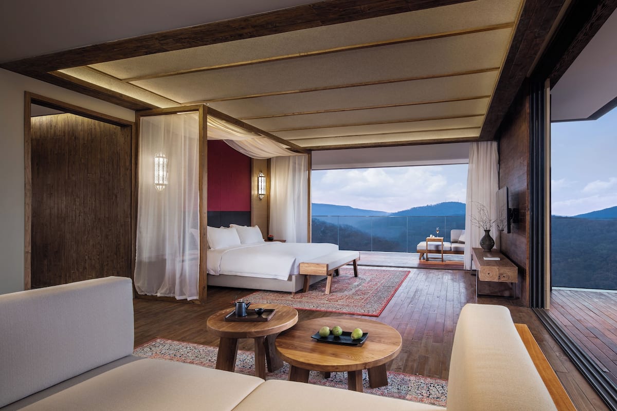 Una camera d'albergo moderna con un letto grande, un divano, un tavolino e un balcone con vista sulle montagne.
