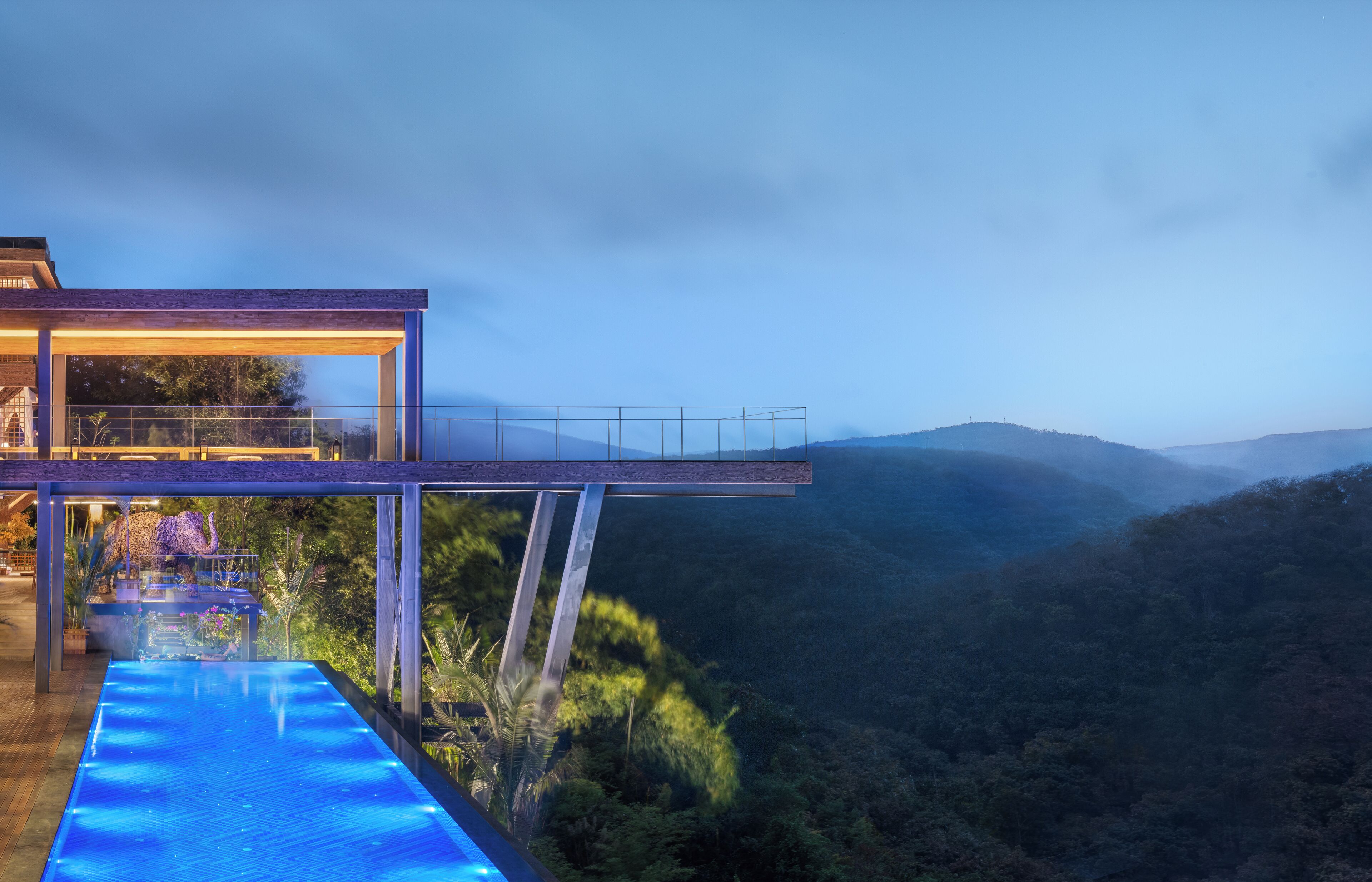 A modern building with a glass balcony overlooking a lush valley.