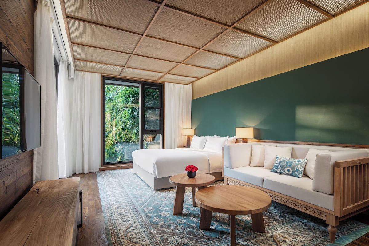 Una camera d'albergo moderna con un letto grande, un divano, un tavolino e vista sul verde dalla finestra.