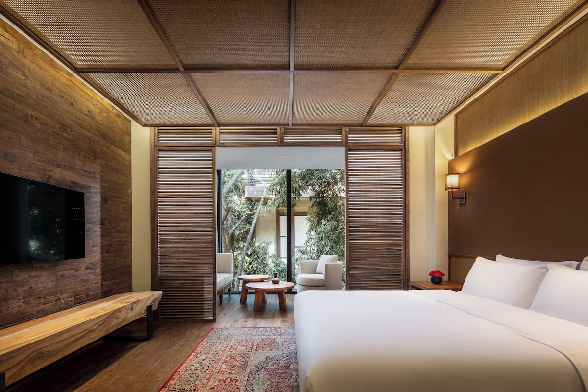 Camera d'albergo moderna con un letto grande, una panca, una TV, un tavolino e vista sul verde attraverso una porta scorrevole.