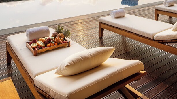 A sunlit outdoor lounge area with wooden flooring, cushioned seating, and a tray of fruits. - Jinghong Bood Panorama Resort Inn (Xishuangbanna Dai)