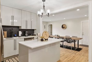 Una cocina moderna con armarios blancos, una isla central y un comedor con mesa y sillas de madera.