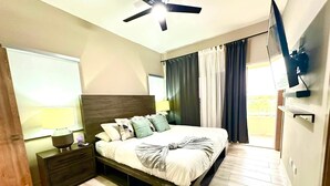 A modern bedroom with a bed, nightstands, a ceiling fan, a TV, and a window with curtains.