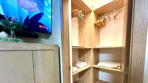A room with a wooden wardrobe, a television displaying a Netflix show, and a wooden closet with hanging clothes.