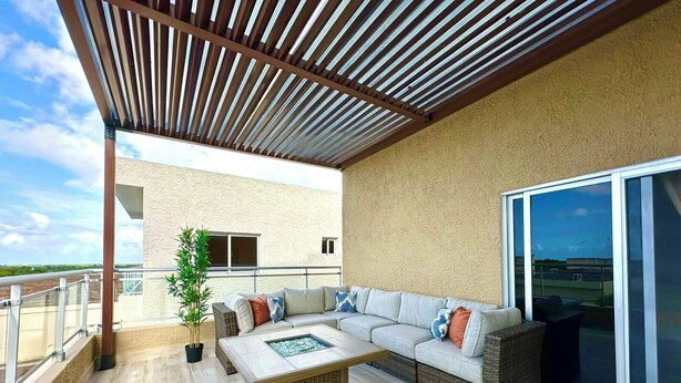 A covered outdoor seating area with a sectional sofa, a coffee table, and a potted plant.