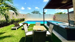 A backyard with a swimming pool, outdoor furniture, and a covered patio area.