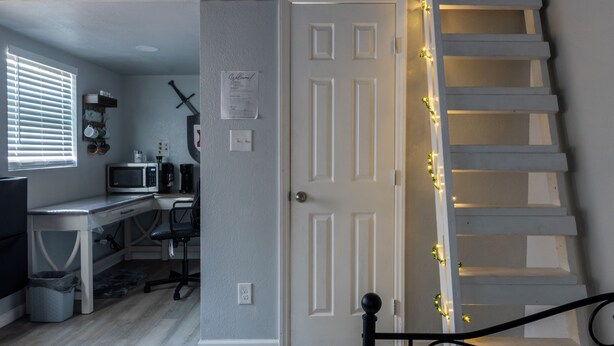 Um quarto com escada, uma escrivaninha com computador e uma porta com placa de 'Welcome'.
