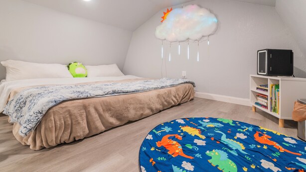A bedroom with a bed, a round ottoman, a bookshelf, and a cloud-shaped light fixture.