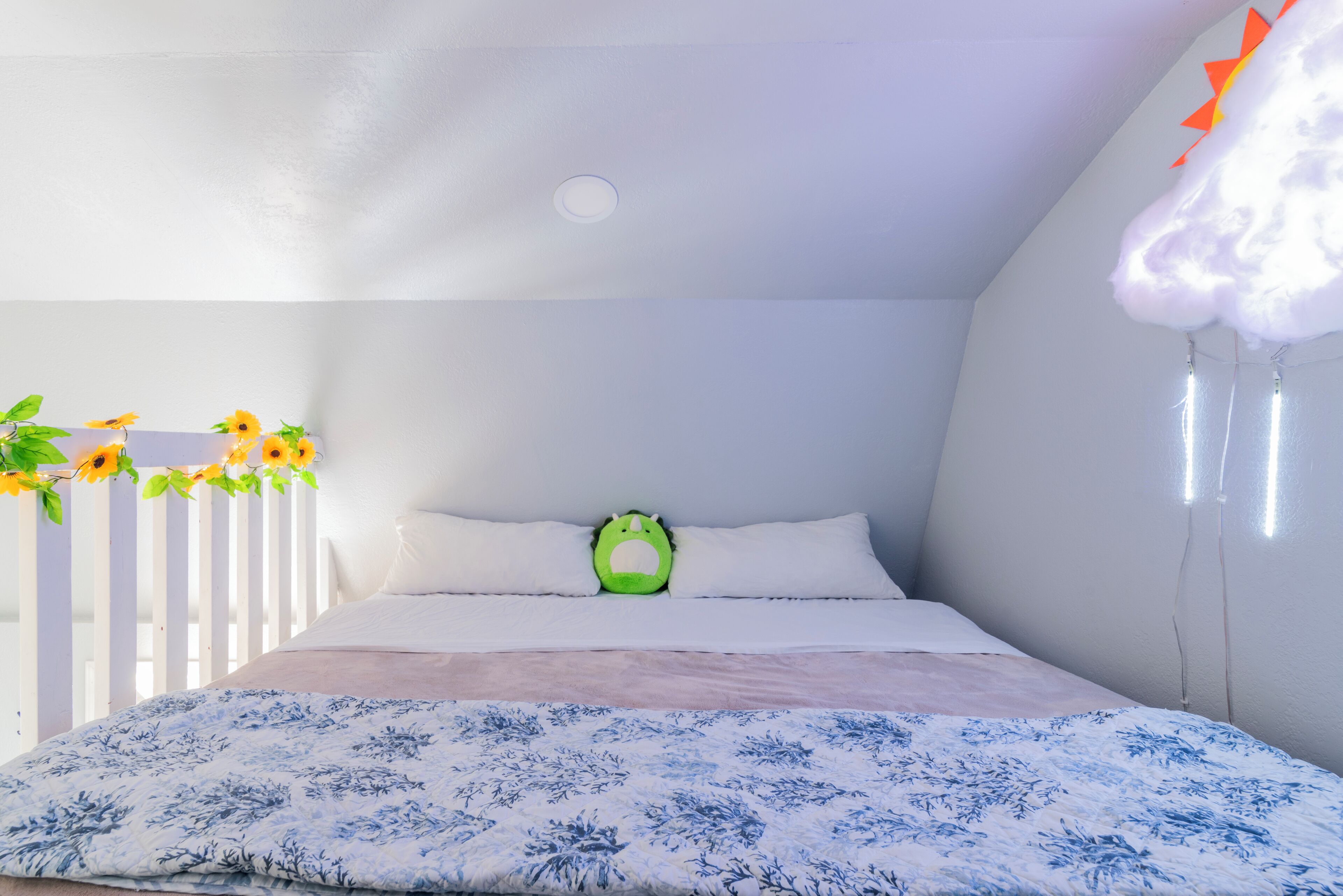 Un dormitorio con una cama, paredes blancas, una lámpara en el techo y una nube decorativa colgando del techo.