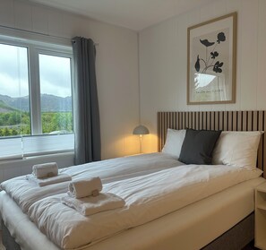 A hotel room with a large bed, a bedside lamp, a framed picture on the wall, and a window with curtains. - Leilighetshotellet AS  (Ålgård)